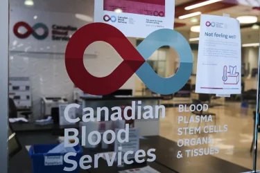 A photo of the Canadian Red Cross logo on a glass wall with a reception desk visible through the glass.